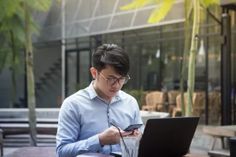 Southeast asian young man using his smartphone and laptop computer in a cafe Stock Photos