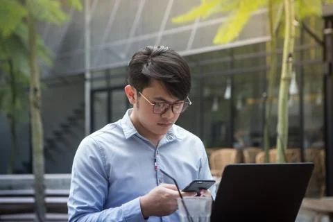 Southeast asian young man using his smartphone and laptop computer in a cafe Stock Photos