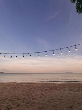 Southern Thai beach at twilight, featuring illuminated string lights, calm .. Stock Photos