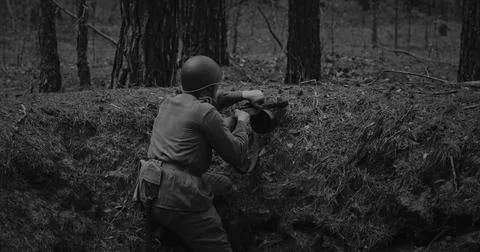 Soviet soldier aims a submachine gun from a forest trench Stock Photos