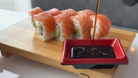 Soy sauce poured into red square dipping dish beside fresh Philadelphia sushi Stock Footage 346183249
