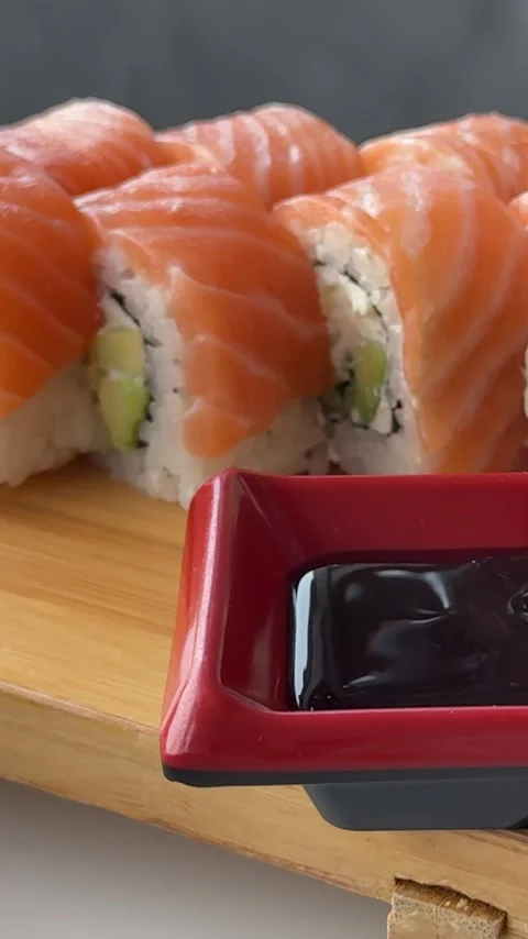 Soy sauce poured into red square dipping dish beside fresh Philadelphia sushi Stock Footage 346183471