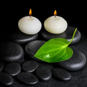 Spa concept of two white candles and green leaf on black zen stones backgroun Foto stock