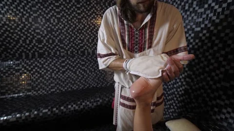 Spa master in a hammam performs a scrub massage of female legs using a kese mitt Stock Footage 157971100
