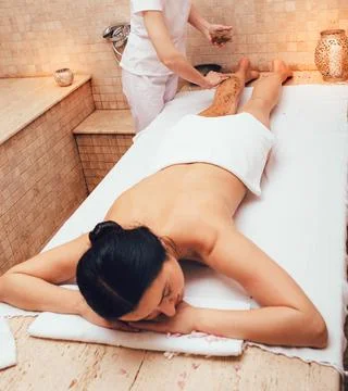 Spa salon worker applying scrub on the legs of a beauty salon client. Exfolia Stockfoto's