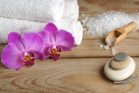 Spa set with white salt for bath, flowers of orchid and towels on a wooden ba Stock Photos