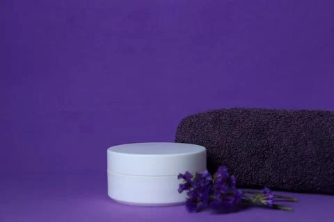 Spa setting with a white container, a dark towel, and lavender on a purple 스톡 사진