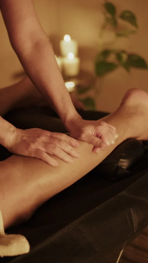 Spa therapist hands massaging client leg with candle light Stock Footage 321030277