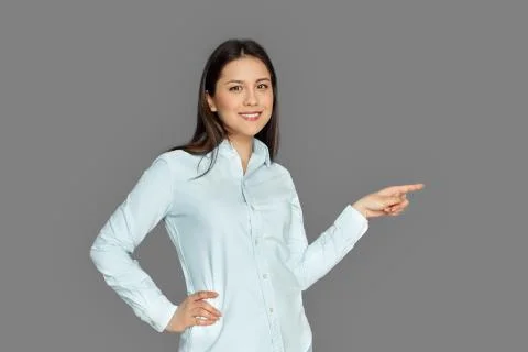 Space for Text or Product. Young woman standing isolated on grey pointing aside Stock Photos