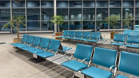 Spacious airport waiting area with empty chairs facing large windows. Stock Illustration