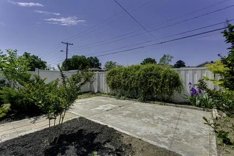 Spacious Backyard With Concrete Patio Surrounded By Greenery And A White Fenc Stock Photos