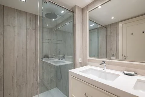 Spacious bathroom with bright artificial lighting, large mirror reflecting front Stock Photos