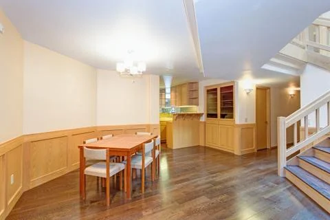 Spacious dining room features white ceiling over a wood dining table surround Stock Photos