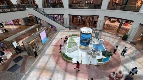 The spacious hall of a Dubai mall features people riding escalators under bri Stock Footage 313388352