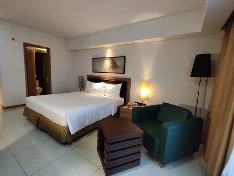A spacious hotel room featuring a large bed with crisp white linens Stock Photos