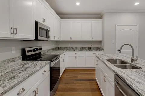 Spacious Kitchen With White Cabinets, Granite Countertops, And Wood Floors. Stock Photos