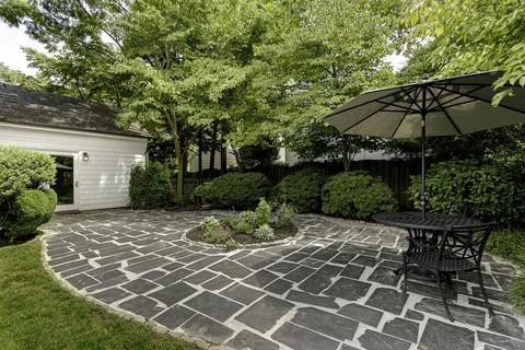 Spacious Patio With Black Table And Umbrella Surrounded By Green Foliage. Stock Photos