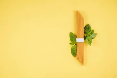 Spaghetti, basil on a yellow background. Top view. Copy space for text. Stock Photos