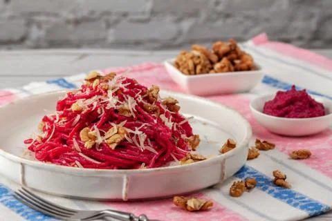Spaghetti with beetroot pesto sauce, walnuts and parmesan on a light backgrou Stock Photos