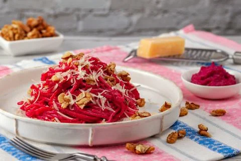 Spaghetti with beetroot pesto sauce, walnuts and parmesan on a light backgrou Stock Photos