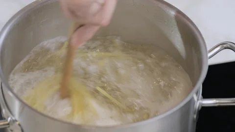 Spaghetti is boiling in a pot, and the cook stirs it with a wooden spoon. Stock Footage 302646507