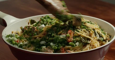Spaghetti with cherry tomato slices and salmon pieces simmering in a pan with Stock Footage 317560667