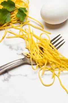 Spaghetti, a fork and an egg on a marble kitchen countertop Stock Photos