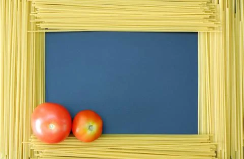 Spaghetti frame with two red tomatoes in corner on dark blue background 스톡 사진