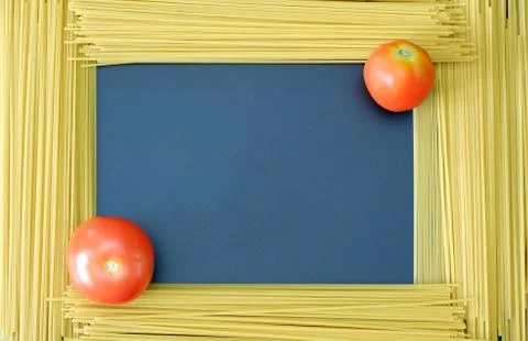 Spaghetti frame with two tomatoes at corners on dark blue background 스톡 사진
