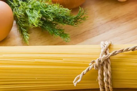 Spaghetti pasta bundle with fresh dill and eggs on wooden surface Stock Photos