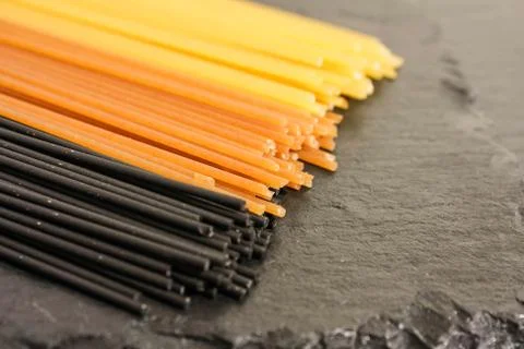 Spaghetti in three colors on a black basalt background Stock Photos