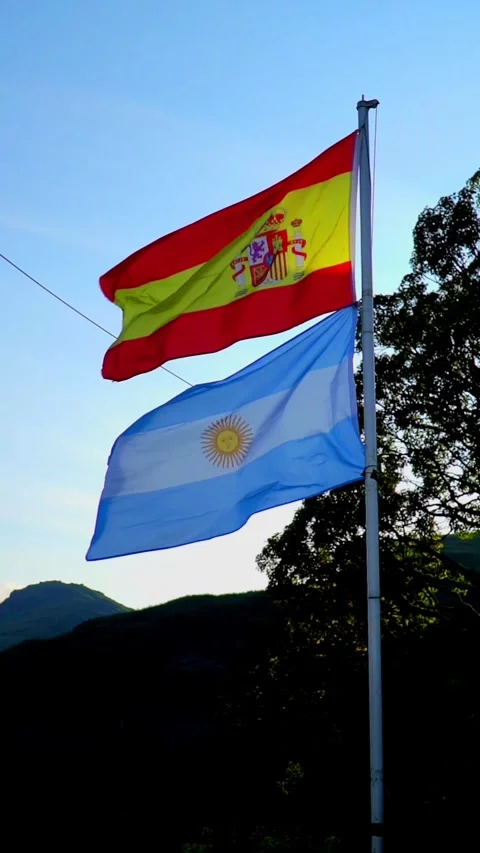 Spanish and Argentine Flags Waving Together on a Flagpole Against a Blue Sky Stock Footage 340097936