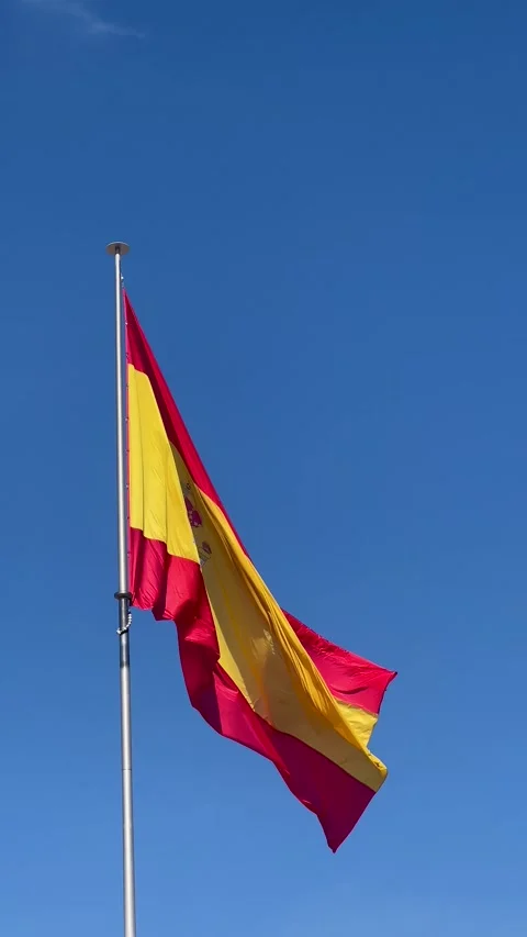 Spanish flag confidently waving on flagpole against pristine blue sky symbol Stock Footage 341383061
