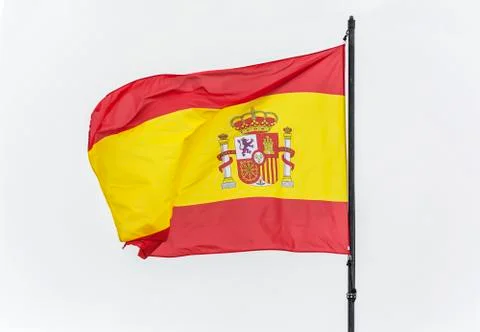 Spanish flag on the flagpole develops in the wind, light background Stock Photos