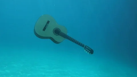 Spanish guitar floating towards the surface of the blue sea Stock Footage 129286158
