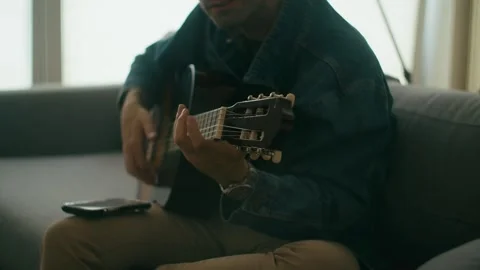 Spanish Guy Playing Classic Guitar On Sofa In Modern Flat Stock Footage 336629577