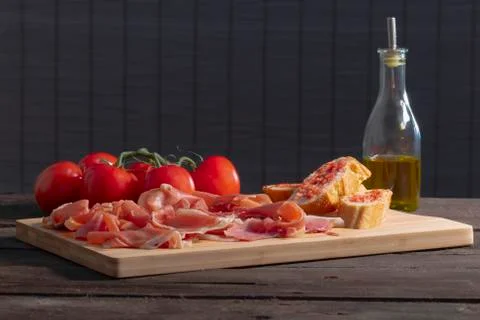 Spanish ham, tomato-rubbed bread, fresh tomatoes and a glass bottle with oliv Stock Photos