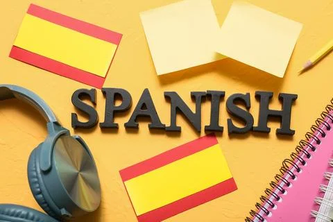 Spanish language learning with headphones, notebook, and flag on yellow backg Stock Photos
