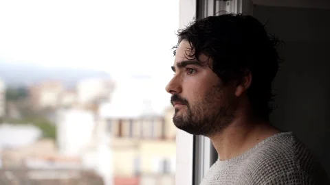 Spanish man drinking from a cup is looking through the window during quaranti 스톡 동영상 129044193