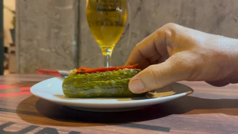 Spanish Tapas: Hand of a Man Wearing Bracelets Eating a Pickle and Drinking a Stock Footage 333558112