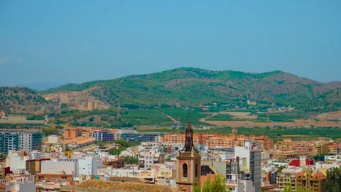 Spanish town beneath green Mediterranean hills with church tower rising above Stock Footage 344868982