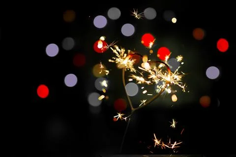 Sparkler in the form of a burning heart surrounded by colorful bokeh Stock Photos