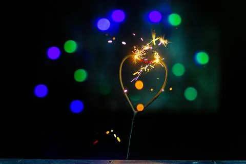 Sparkler in the form of a burning heart surrounded by colorful bokeh Stock Photos