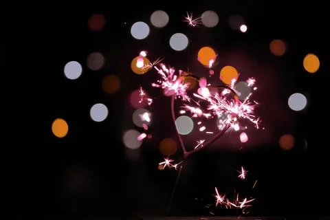Sparkler in the form of a burning heart surrounded by colorful bokeh Stock Photos