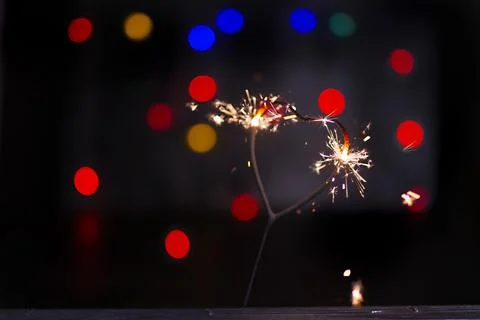 Sparkler in the form of a burning heart surrounded by colorful bokeh Stock Photos
