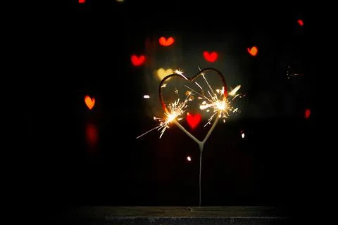 Sparkler in the form of a burning heart surrounded by colorful bokeh Stock Photos