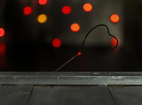 Sparkler in the form of a burning heart surrounded by colorful bokeh Stock Photos