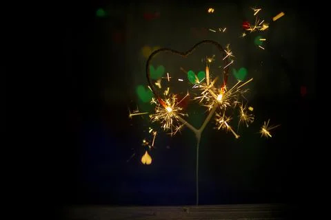 Sparkler in the form of a burning heart surrounded by colorful bokeh Stock Photos