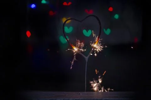 Sparkler in the form of a burning heart surrounded by colorful bokeh Stock Photos
