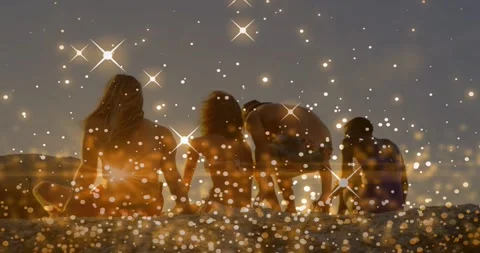 Sparkles appearing at sunset, four figures sitting on sand, third leaning, Video stock 331833520